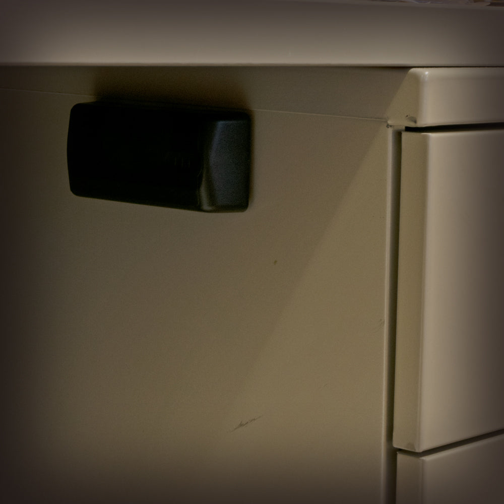 Master Lock black magnetic key hider shown hidden under neath a metal desk