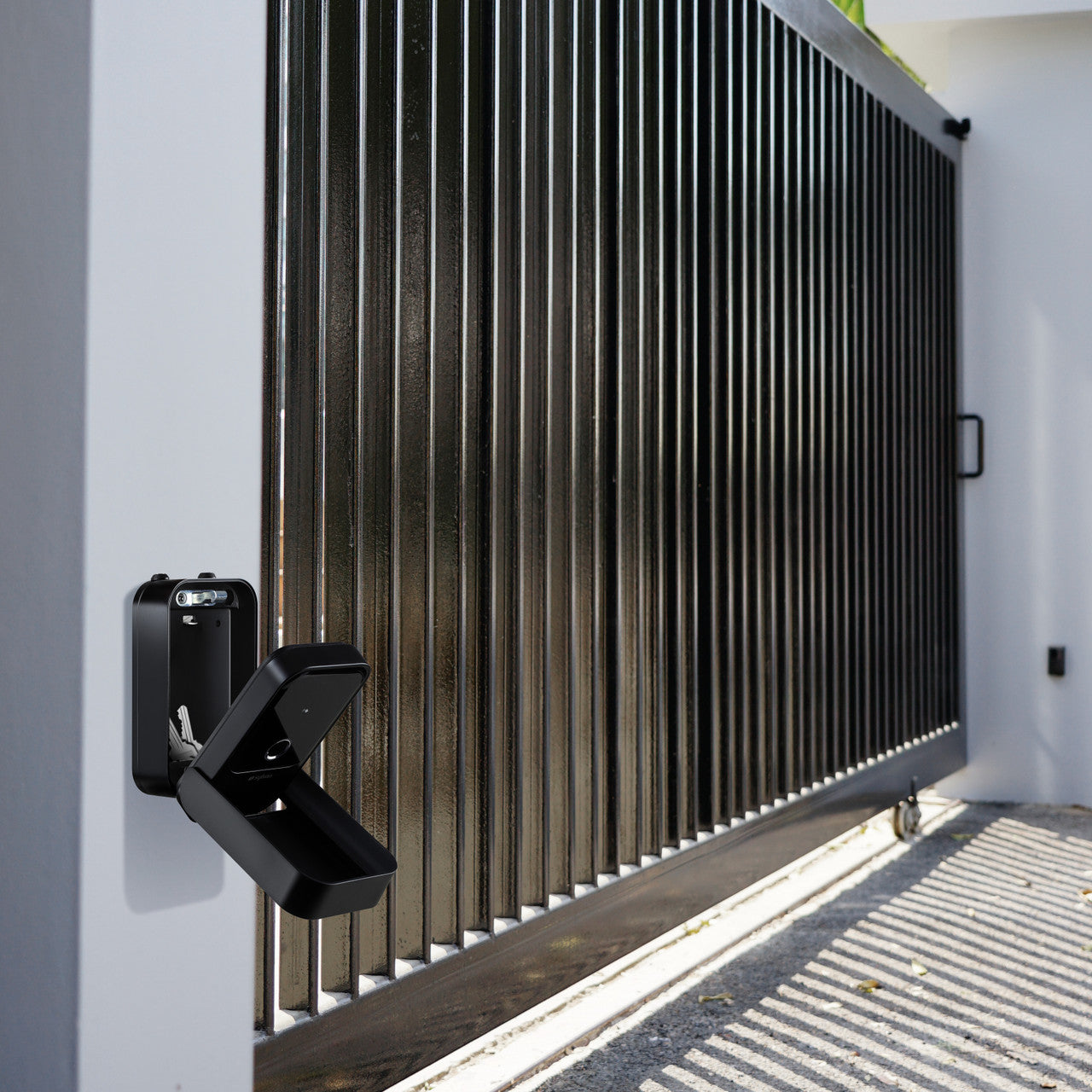 Sylvan Bluetooth black lock box shown open attached to a wall next to a sliding gate entry