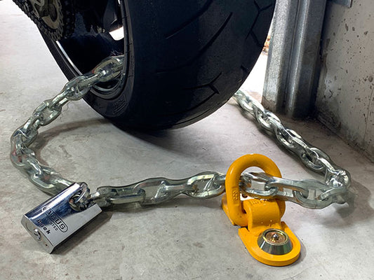 Pitbull yellow floor anchor fixed to a concrete floor with metal chain & padlock around a tyre