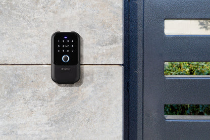 Sylvan Bluetooth black touchscreen lock box attached to a concrete wall next to a gate