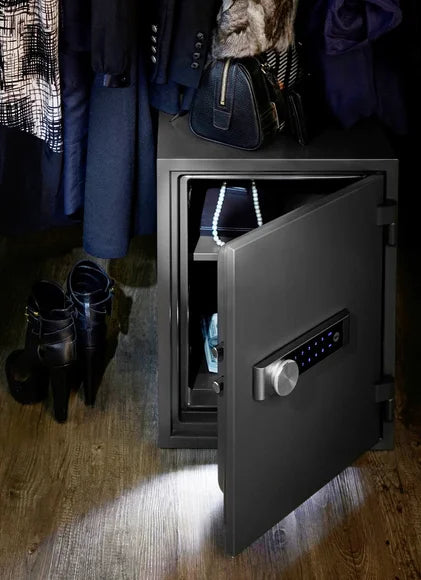 Black safe with open door on a wooden floor next to shoes and clothing.