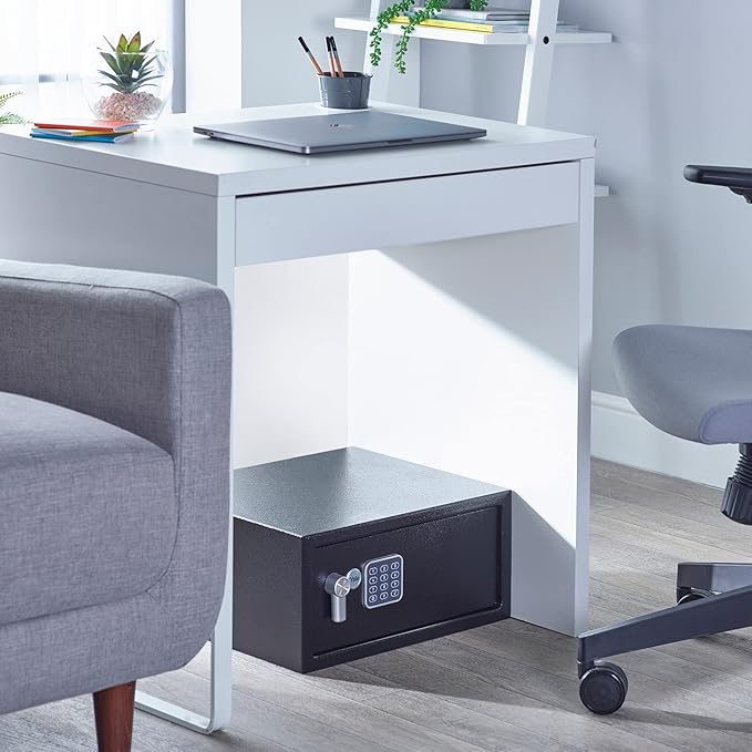Black safe box under a white desk with gray chairs in a room.