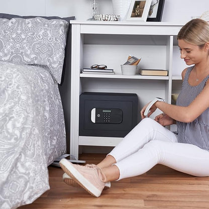 Woman sitting on the floor next to a bed with a safe box underneath a shelf.