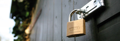 Abus brass padlock attached through a hasp & staple on a black wooden fence
